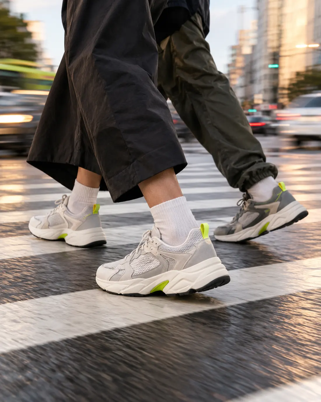 Two pairs of feet in sneakers on a zebra crossing with the city blurred behind