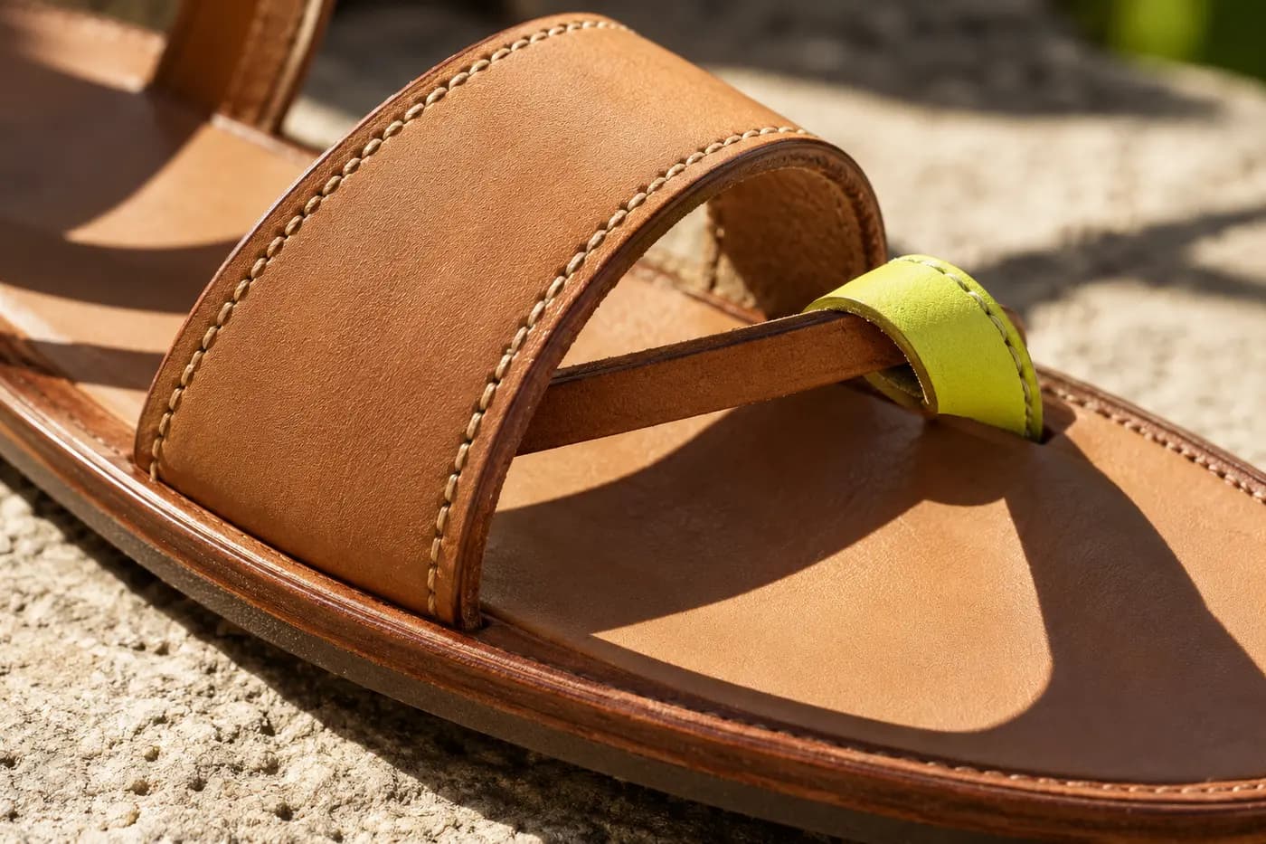 Macro of a leather sandal strap with stitching and a lime toe post